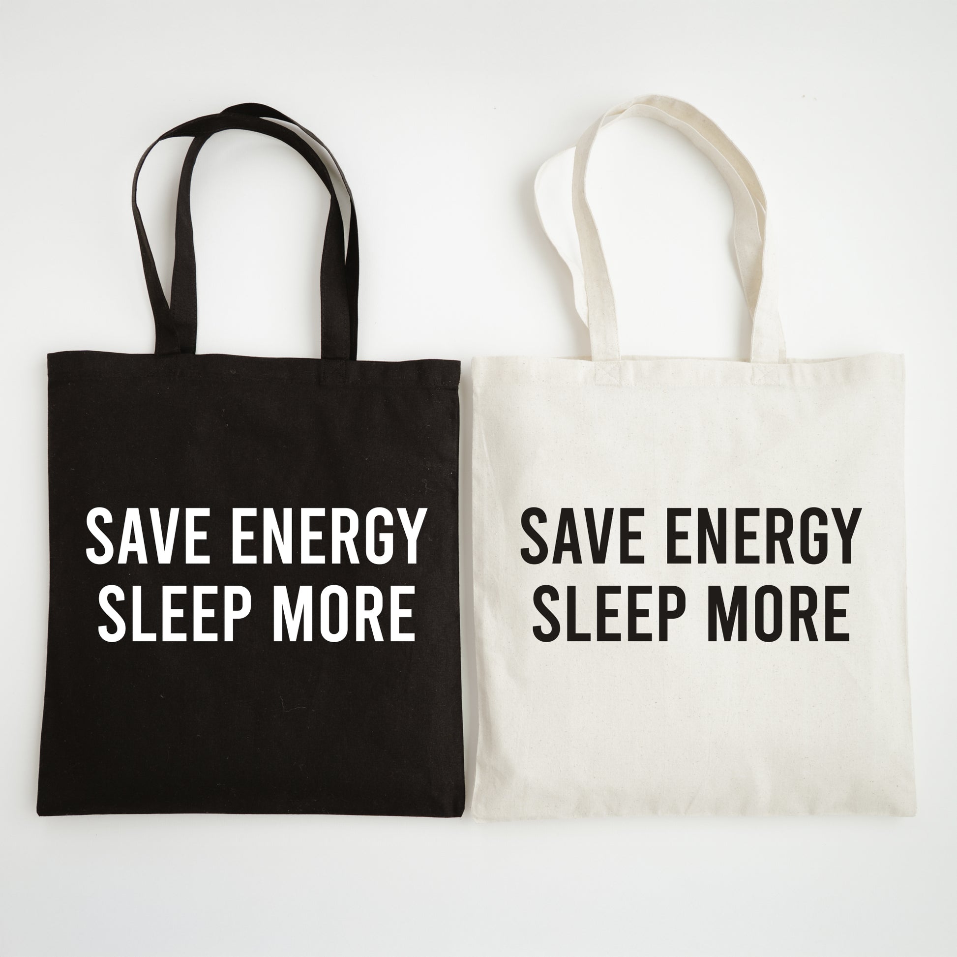 Black and white tote bags with 'SAVE ENERGY SLEEP MORE' text on a light gray background