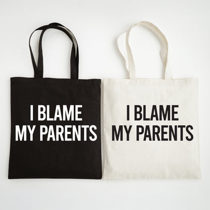 Two tote bags, one black and one white, with 'I Blame My Parents' text on a light gray background.