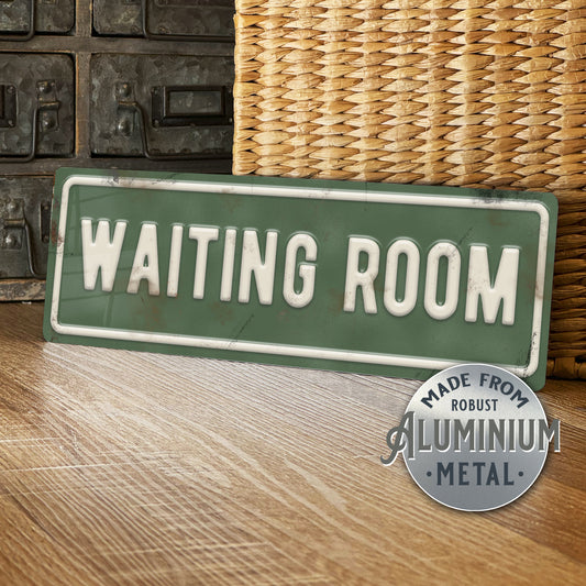 Green 'WAITING ROOM' sign with metallic finish on a wooden surface.