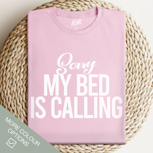 Pink t-shirt with 'Sorry My Bed Is Calling' text on a woven surface