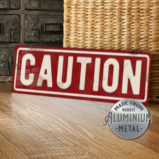 Red and white 'CAUTION' sign with metallic finish on a wooden surface.