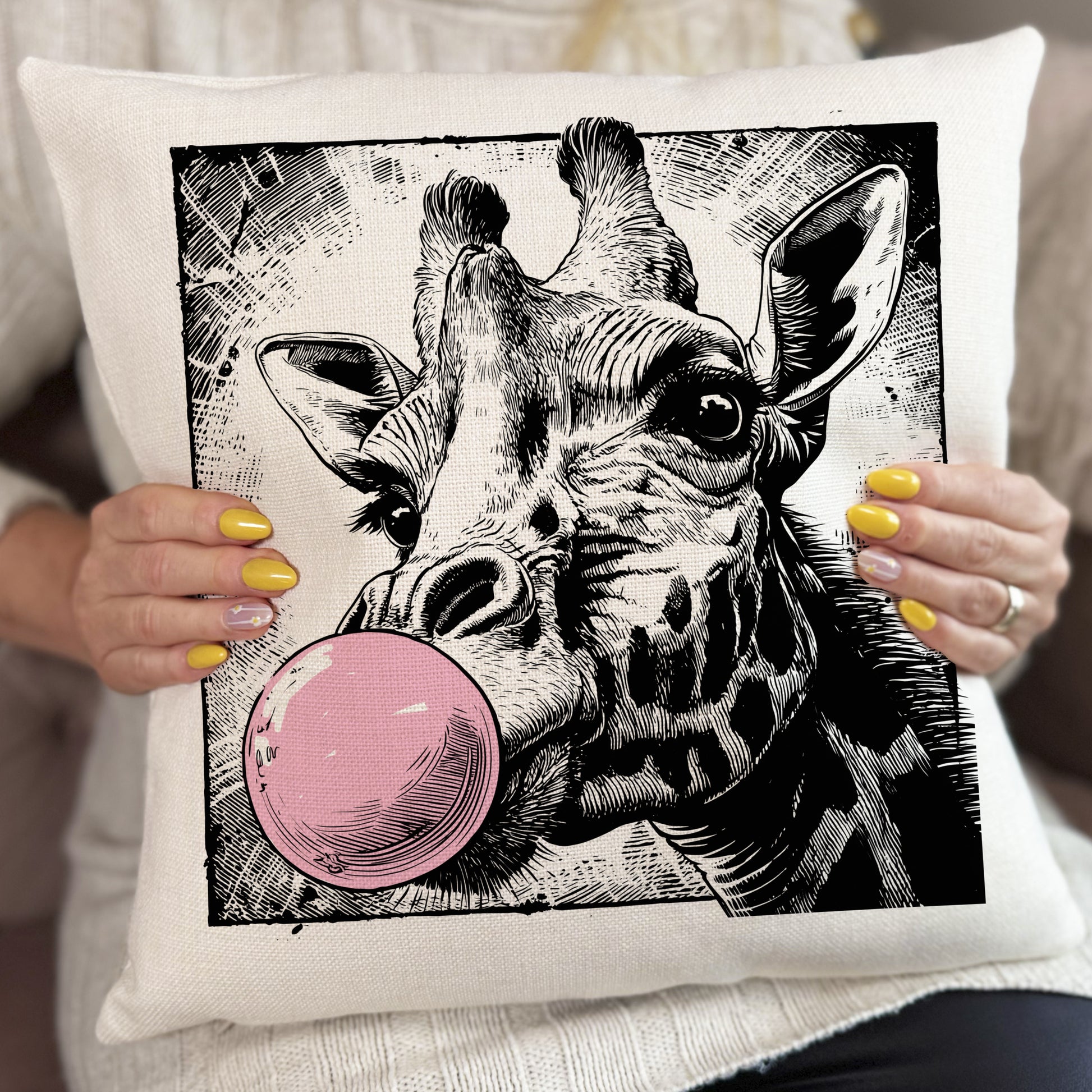 Pillow with a giraffe illustration blowing a pink bubble, held by a person.