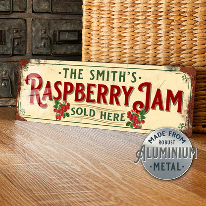 Vintage-style sign reading 'The Smith's Raspberry Jam Sold Here' on a wooden surface with a wicker basket in the background.
