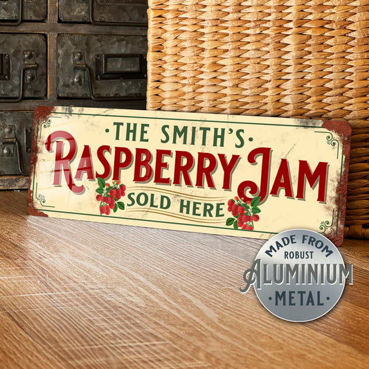 Vintage-style sign reading 'The Smith's Raspberry Jam Sold Here' on a wooden surface with a wicker basket in the background.
