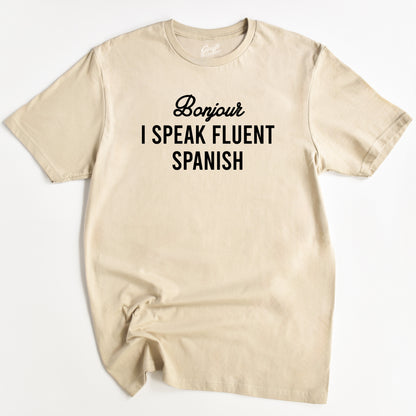 Sand T-shirt with the text 'Bonjour I SPEAK FLUENT SPANISH' printed in Black.